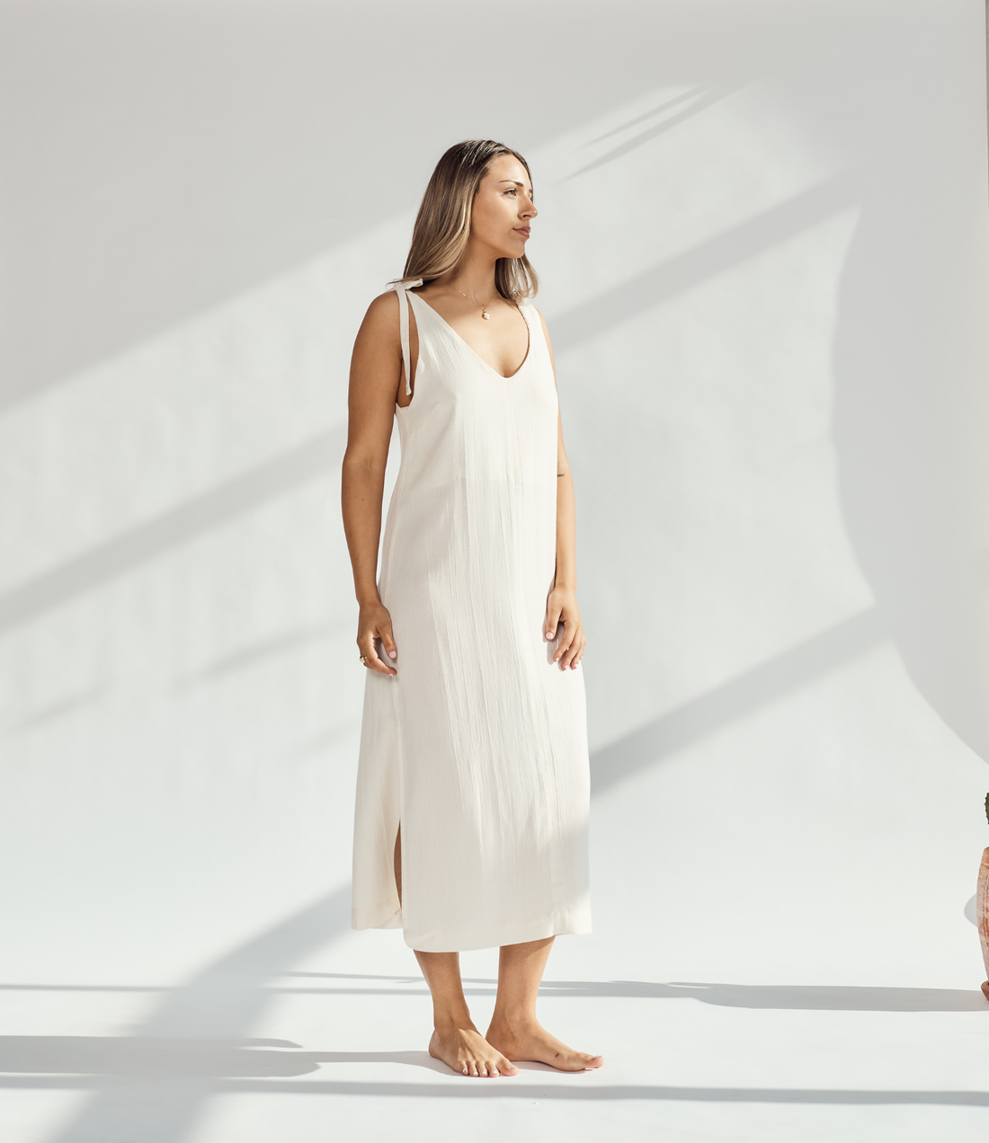 Elegant soft cotton dress with tied straps and leg slits, worn by a woman standing gracefully.