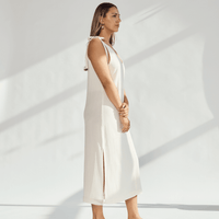 Side view of a woman in a soft cotton dress with tied straps and leg slits against a light background.