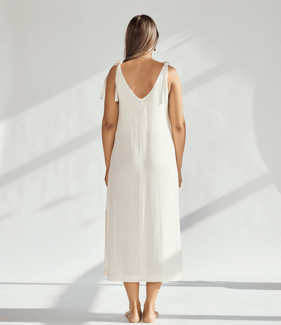 Back view of a woman wearing a soft cotton dress with tied straps, showcasing its elegant, breathable design.