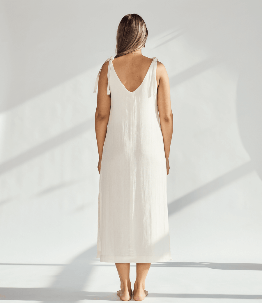 Back view of a woman wearing a soft cotton dress with tied straps, showcasing its elegant, breathable design.