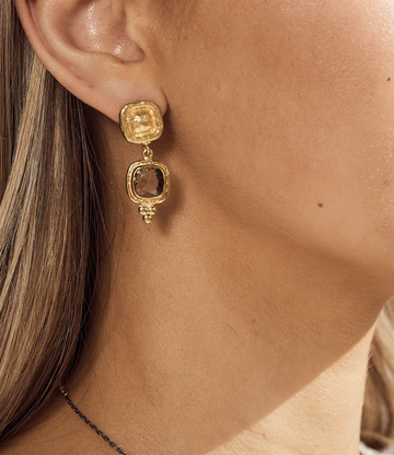 Gold earrings worn by a person with a neutral background