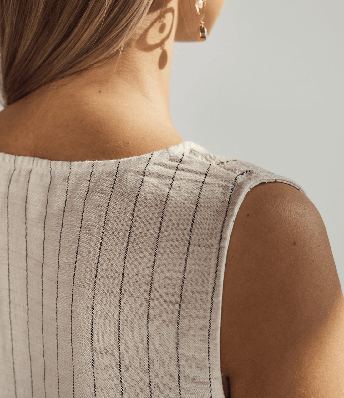 Close-up of a person wearing a sleeveless top with black pinstripes on a neutral background