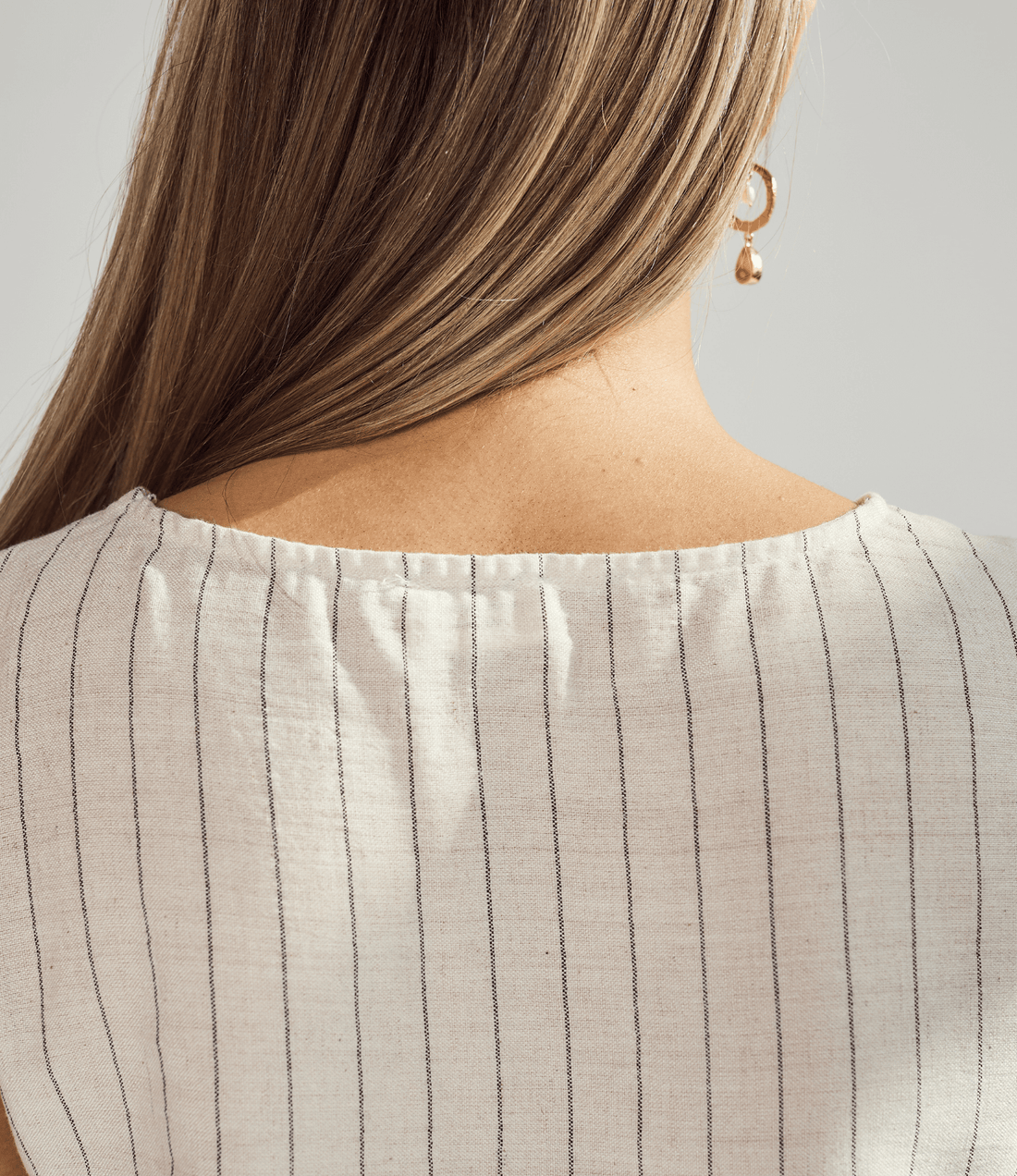 Close-up of a person wearing a beige pinstripe top with a plain background