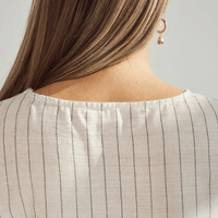 Close-up of a person wearing a beige pinstripe top with a plain background