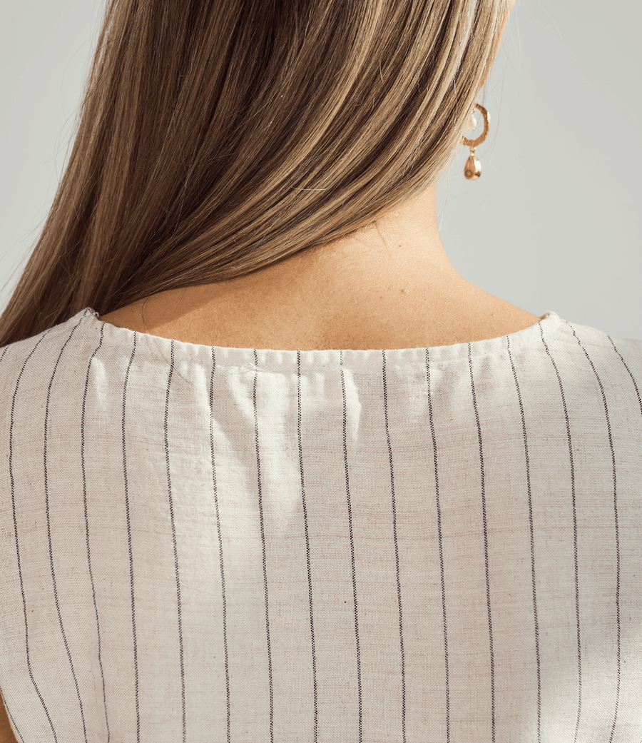 Close-up of a person wearing a beige pinstripe top with a plain background
