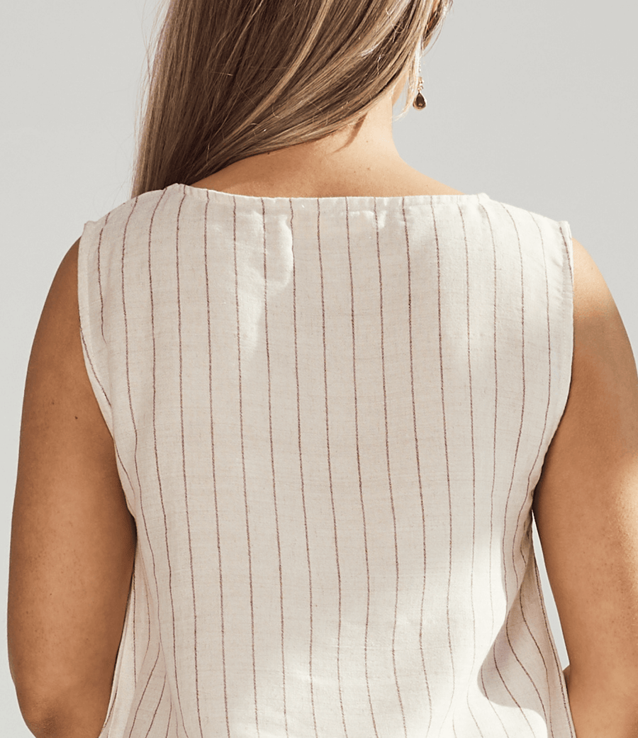 Close-up of a person wearing a beige sleeveless top with thin vertical stripes on a light gray background.