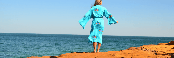 Model on top of red cliff wearing blue Evil eye robe